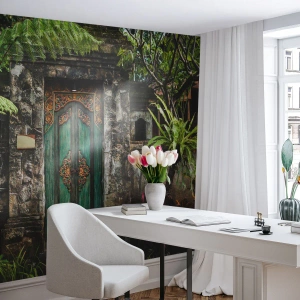 Fototapeta Standard Eco - Zdobené dřevěné dveře zasazené mezi tropickou vegetaci a kamennou zdí - 100x70cm - Dveře do exotického světa - Moderní nástěnná dekorace do obývacího pokoje a ložnice ARTTOR